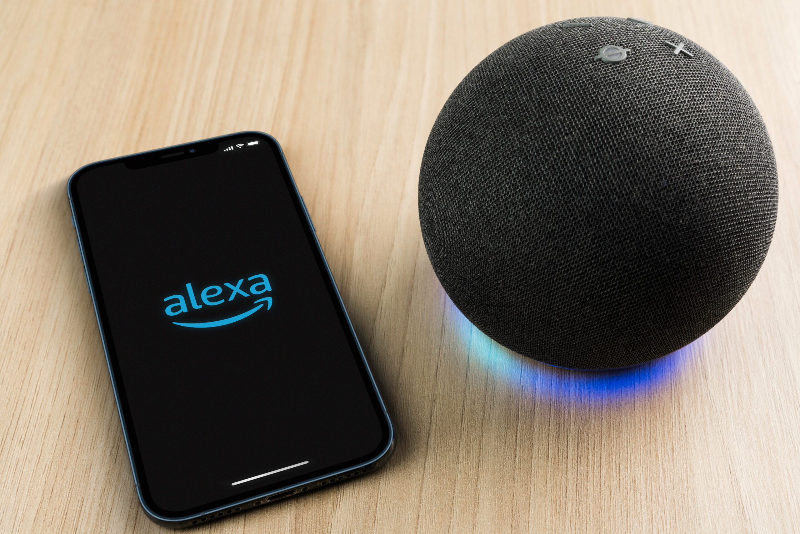 Alexa, Smart speaker and virtual assistant from Amazon company connected to smartphone app. Wooden background.